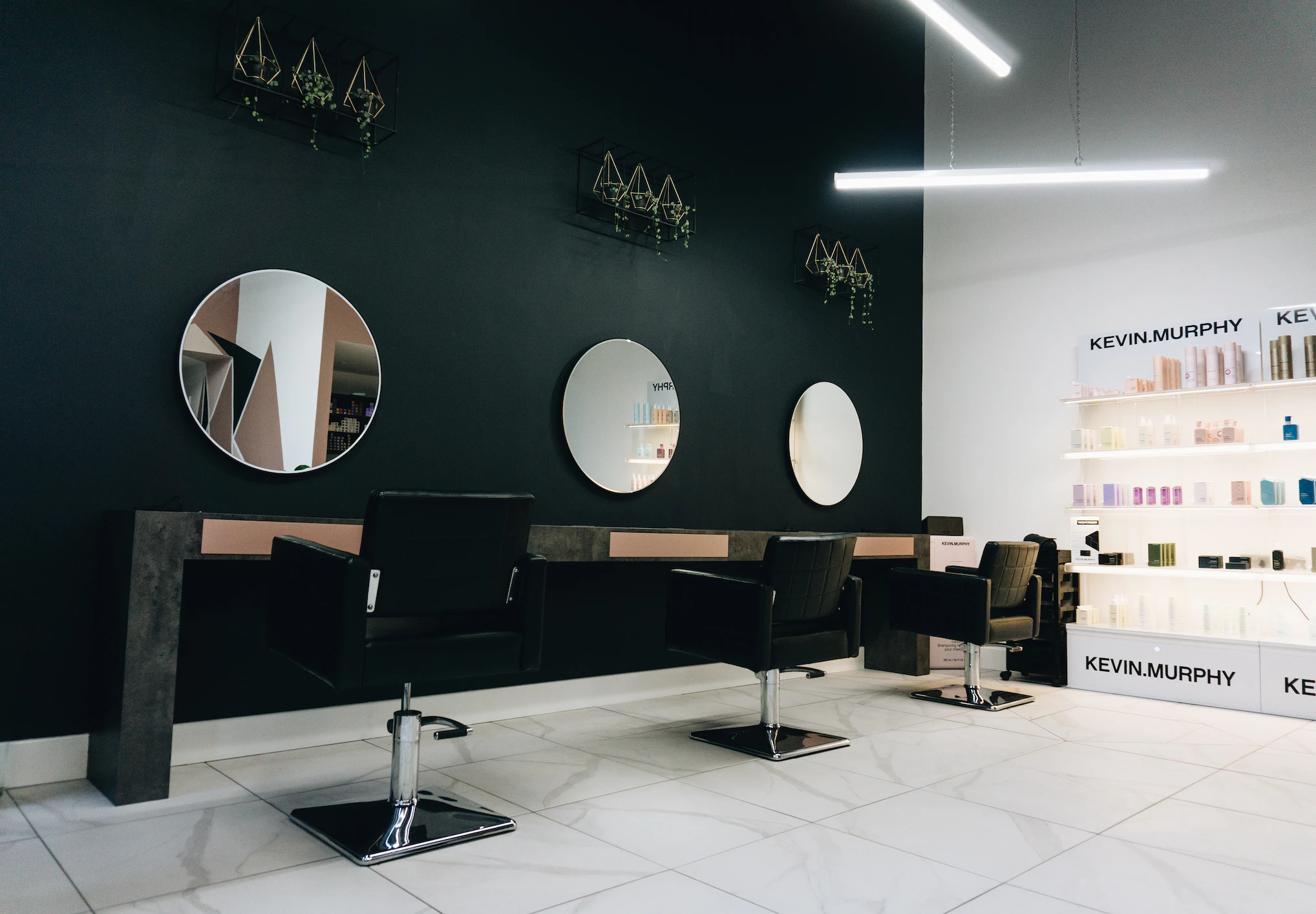 Salon de coiffure : trois fauteuils devant des miroirs ronds, étagères de produits éclairées